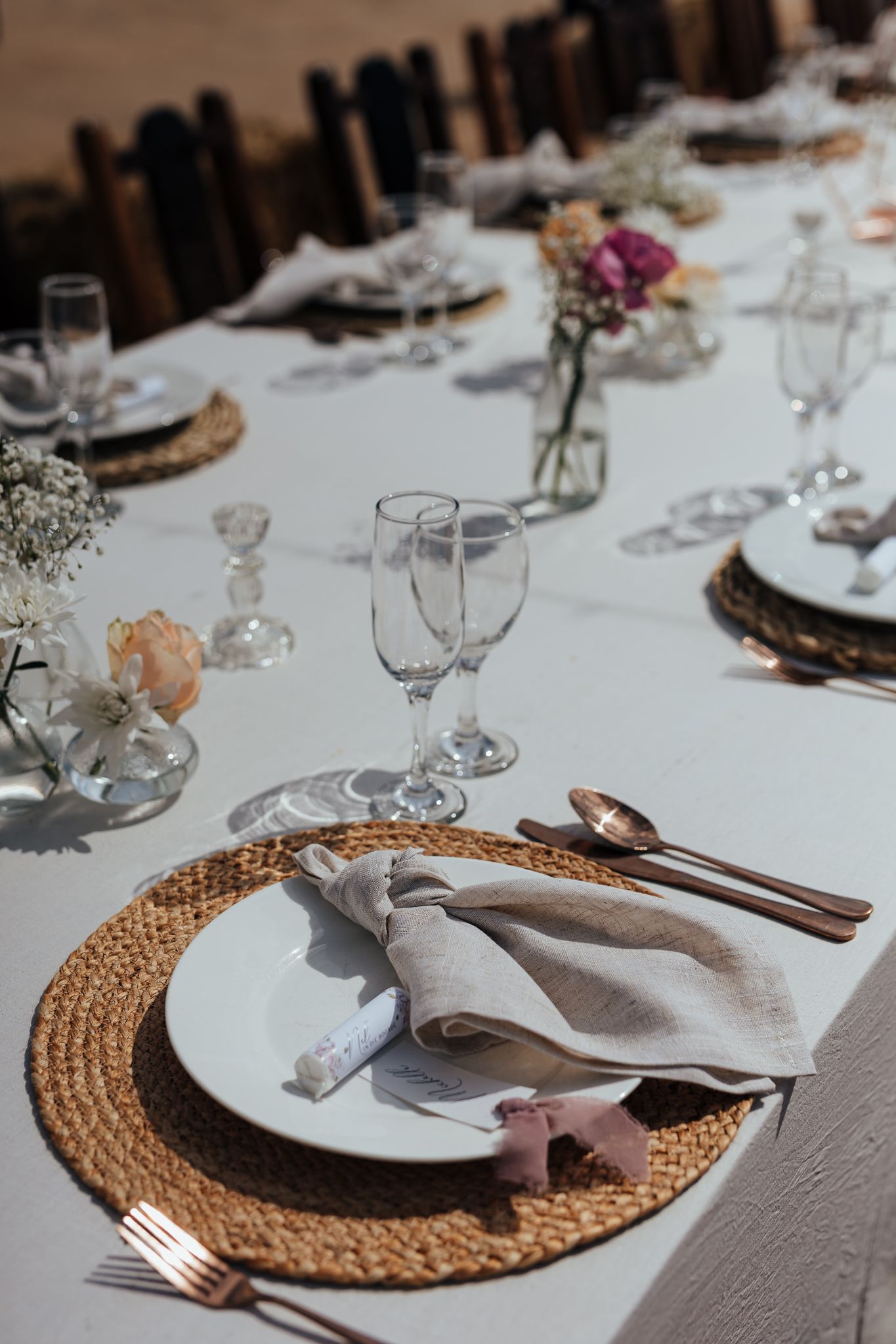 Wedding table setting with white linens, woven chargers, and delicate floral centerpieces.