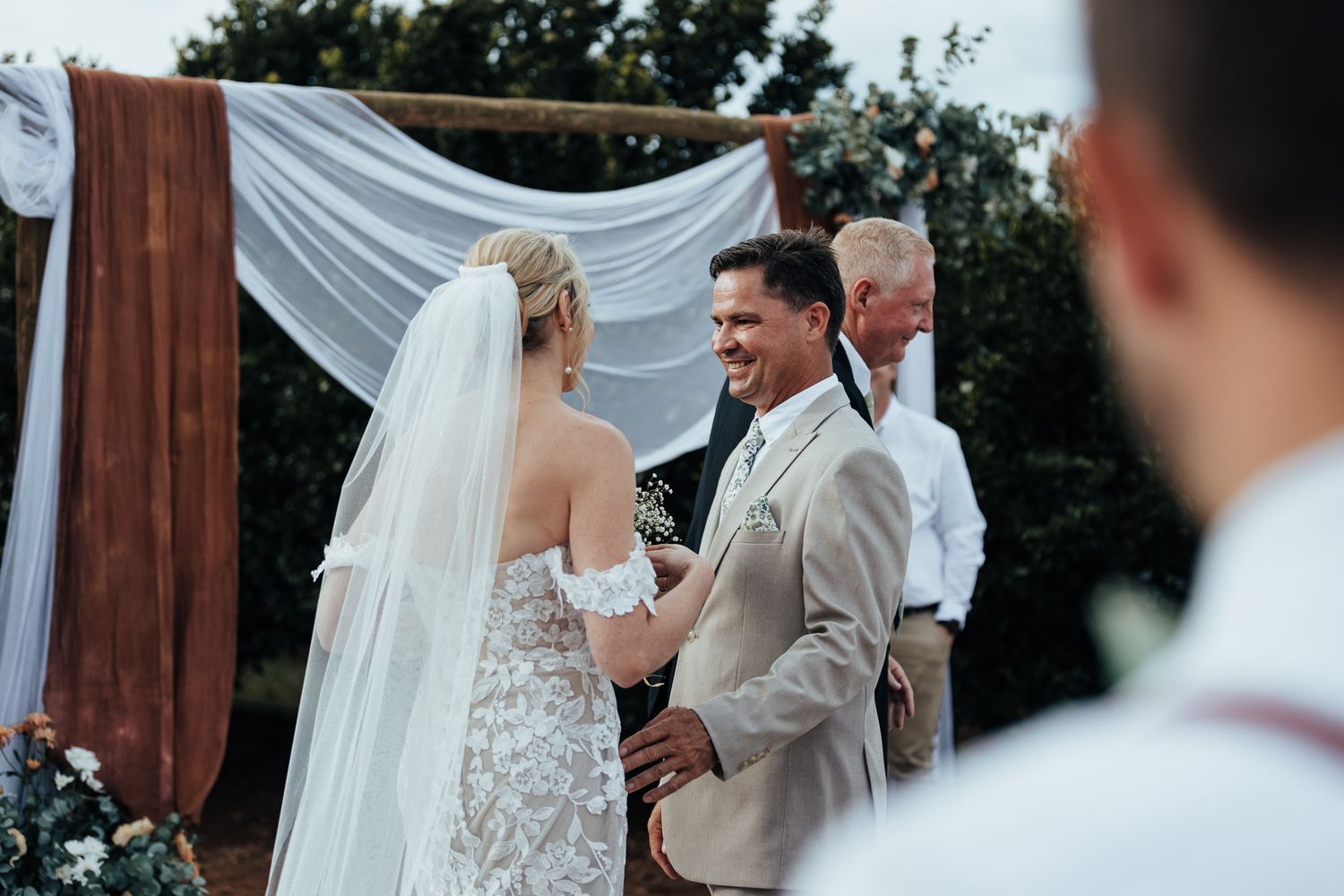 Couple exchanging vows at rustic outdoor wedding ceremony with white draped fabric altar.