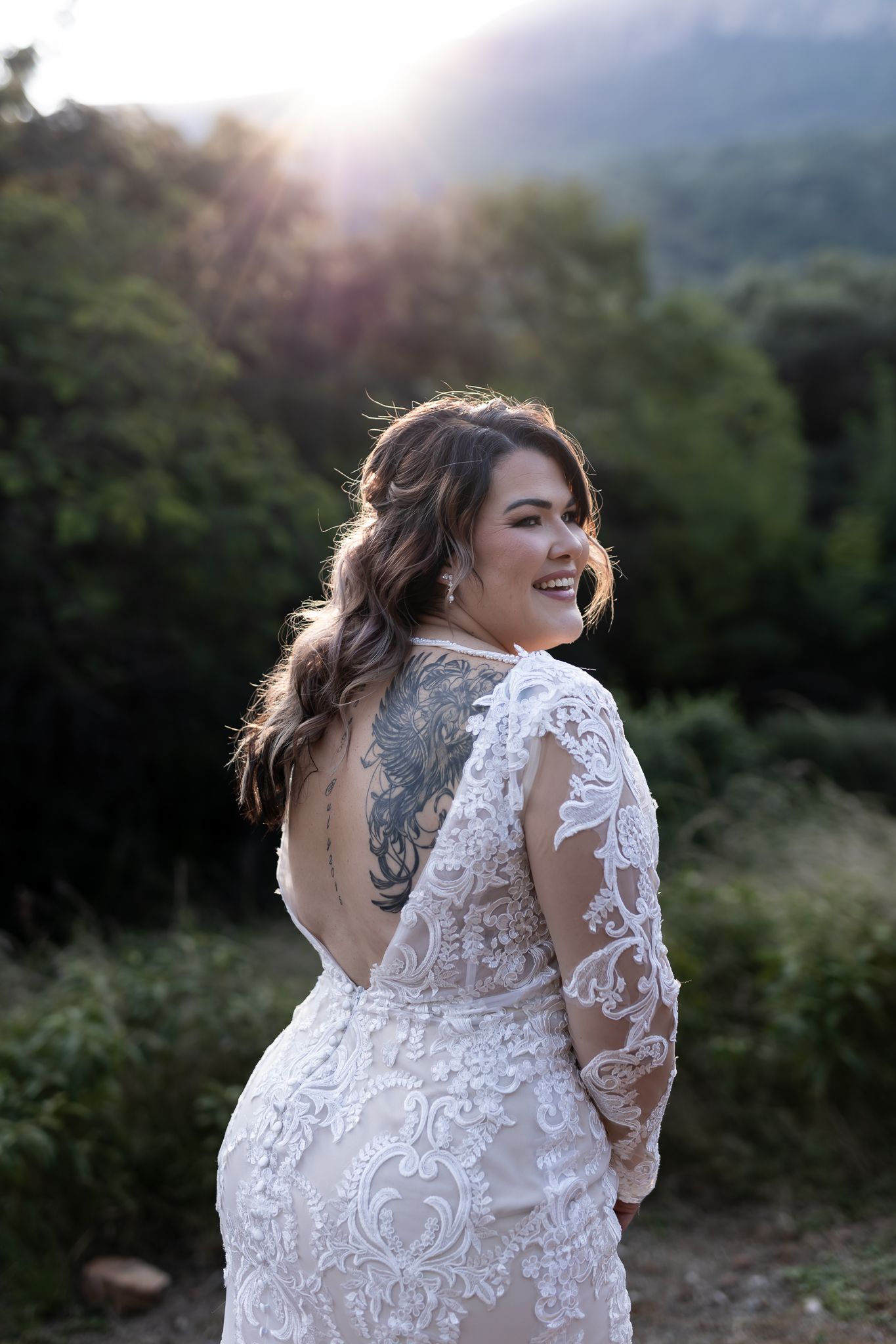 Joyful bride in lace dress laughs during sunset portrait session.