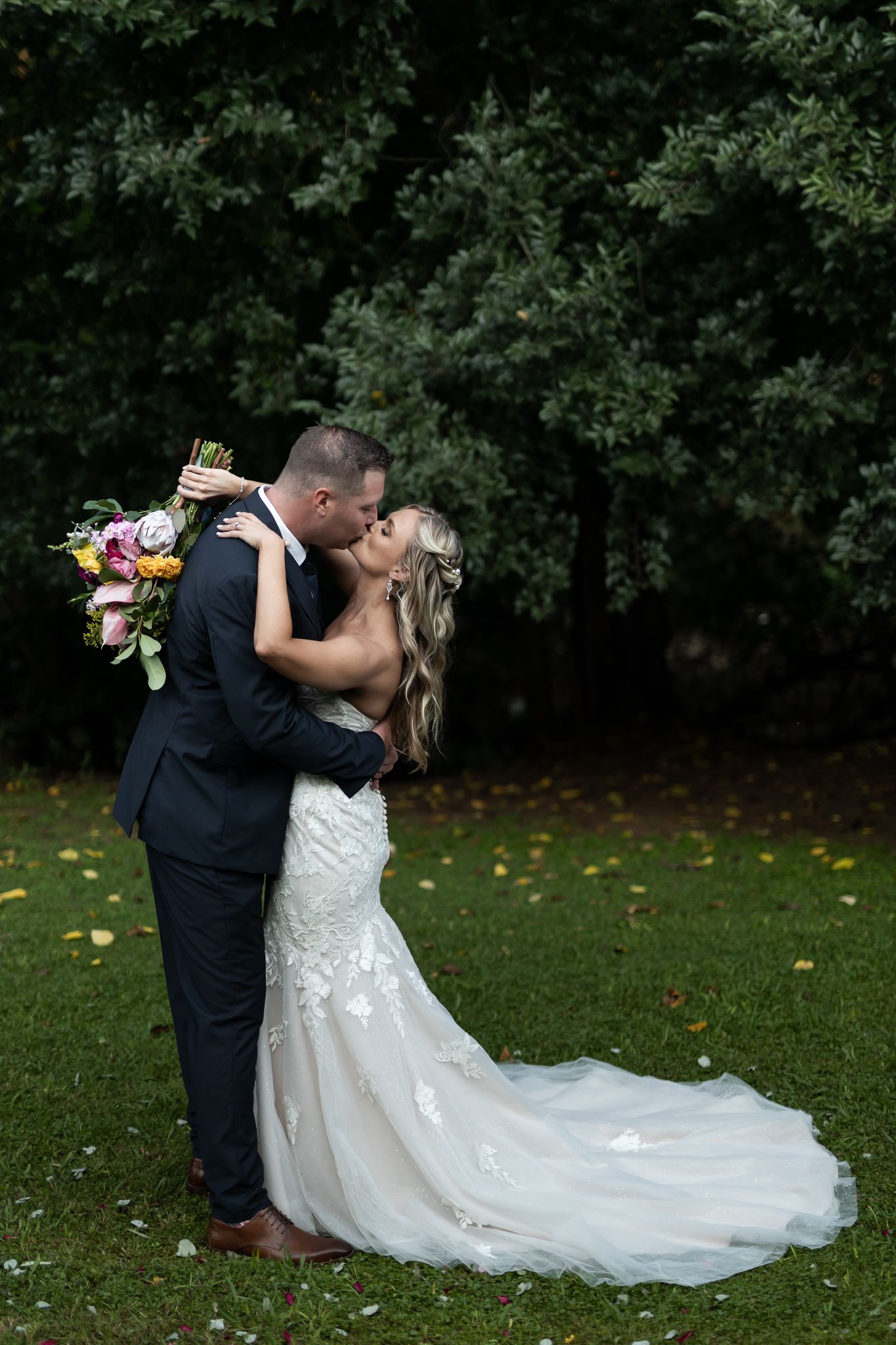 Romantic wedding portrait of couple kissing on lawn with bride's dress trailing behind.