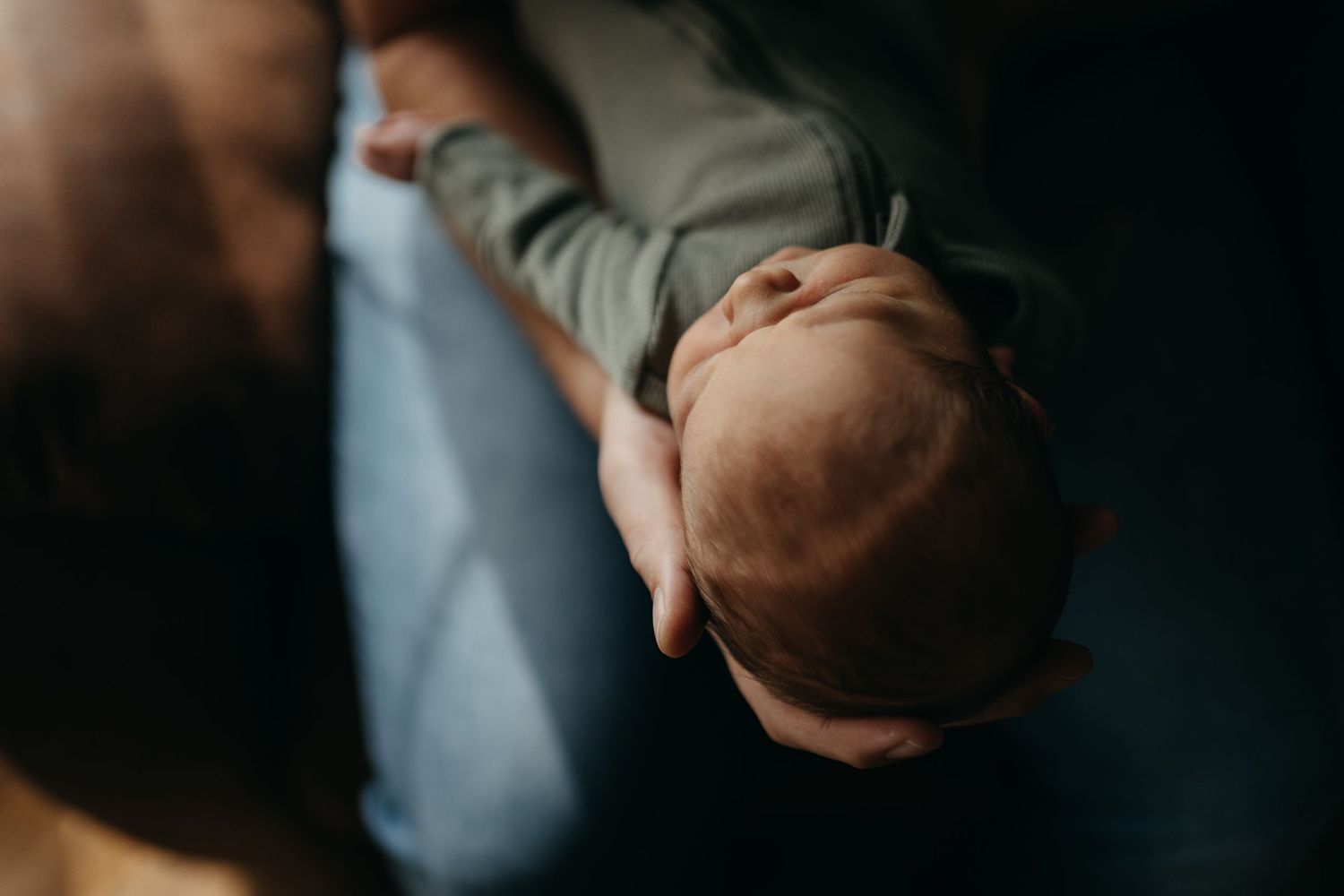 A tender moment between a parent and newborn baby in soft, natural lighting against a dark background.