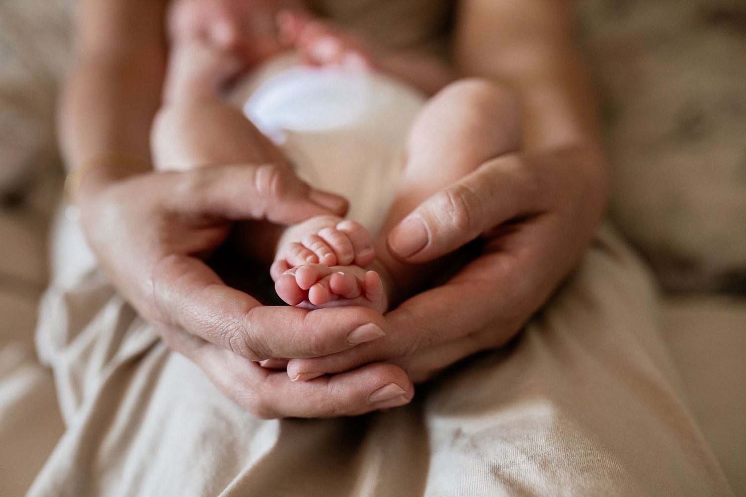 Close-up details of tiny newborn baby hands and feet being gently held against a neutral background.