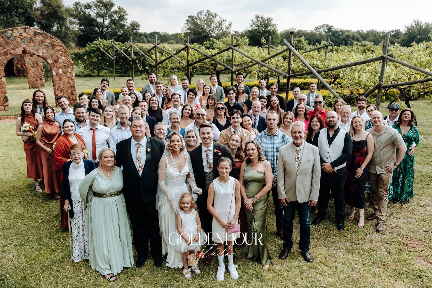 Large group wedding photo of guests and wedding party on a sunny outdoor lawn.