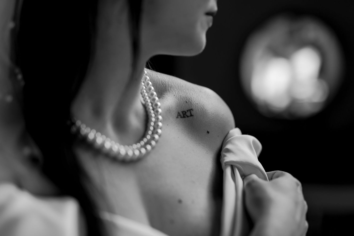 Black and white close-up shot showing a pearl necklace and bare shoulder in dramatic lighting.