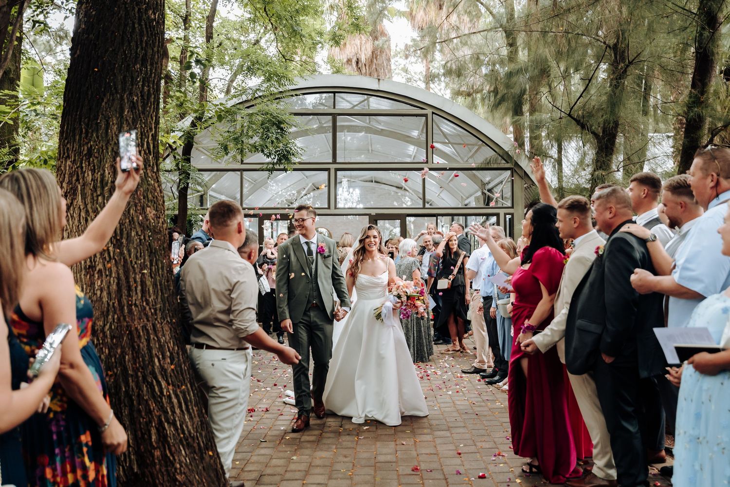 Outdoor wedding ceremony among tall trees with guests gathered to celebrate.