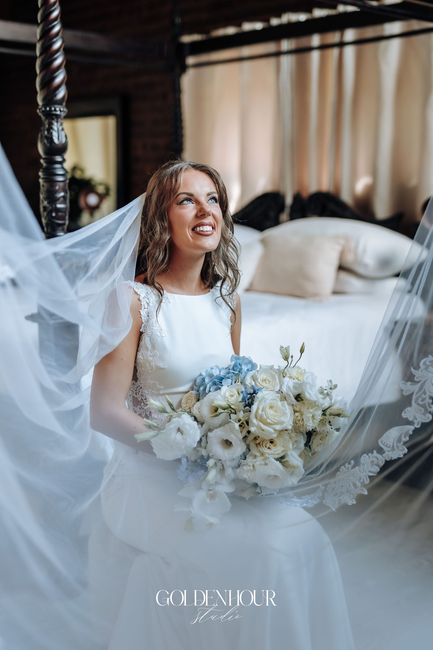 Elegant bridal portrait with flowing veil and white and blue floral bouquet.
