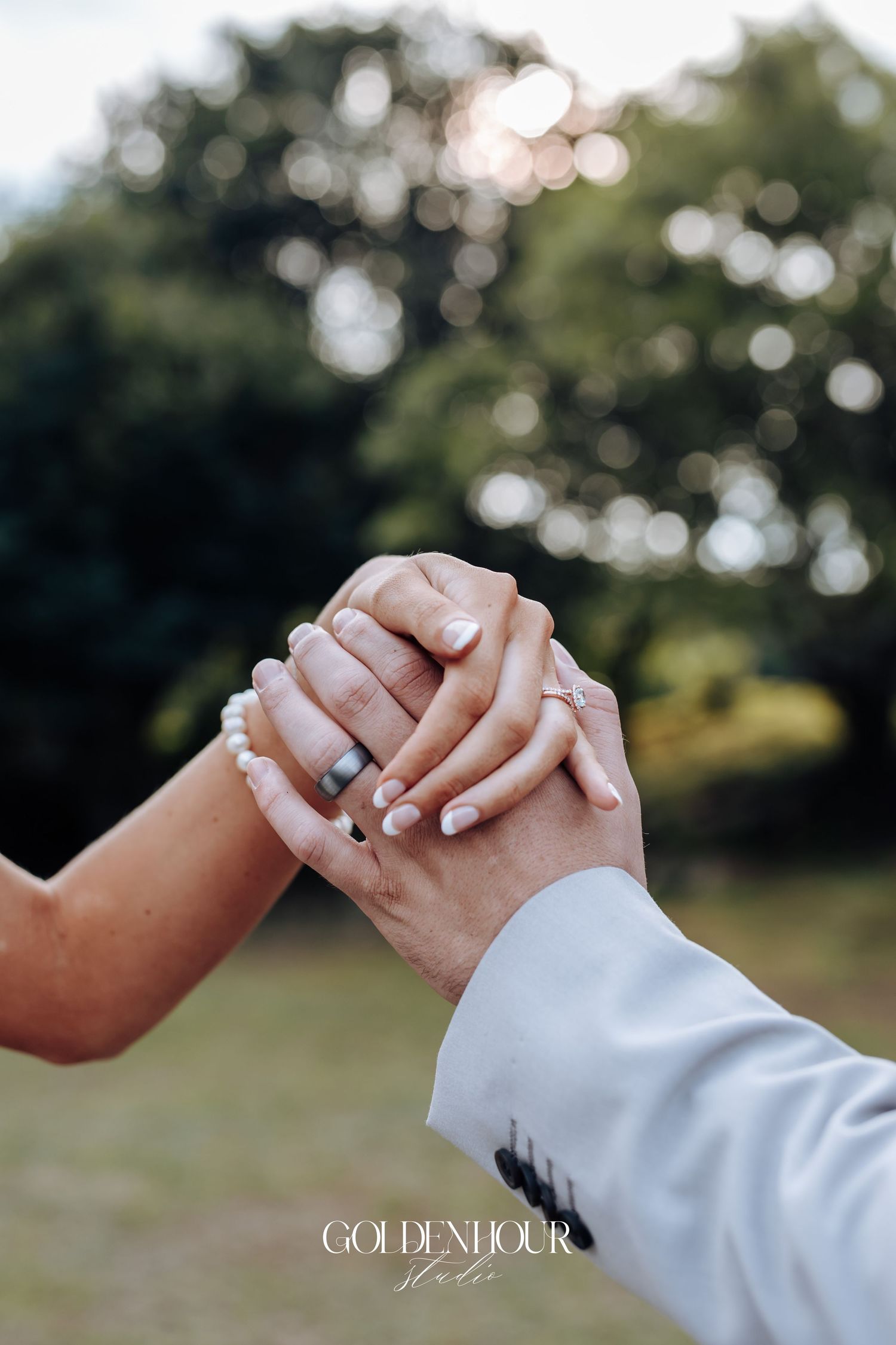 Close-up of newlywed couple's hands with wedding rings intertwined against soft natural background.