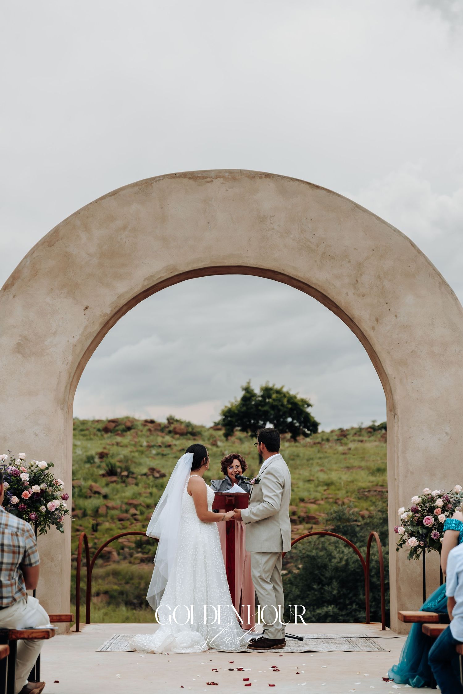 Stone archway frames an outdoor wedding ceremony against a natural landscape.