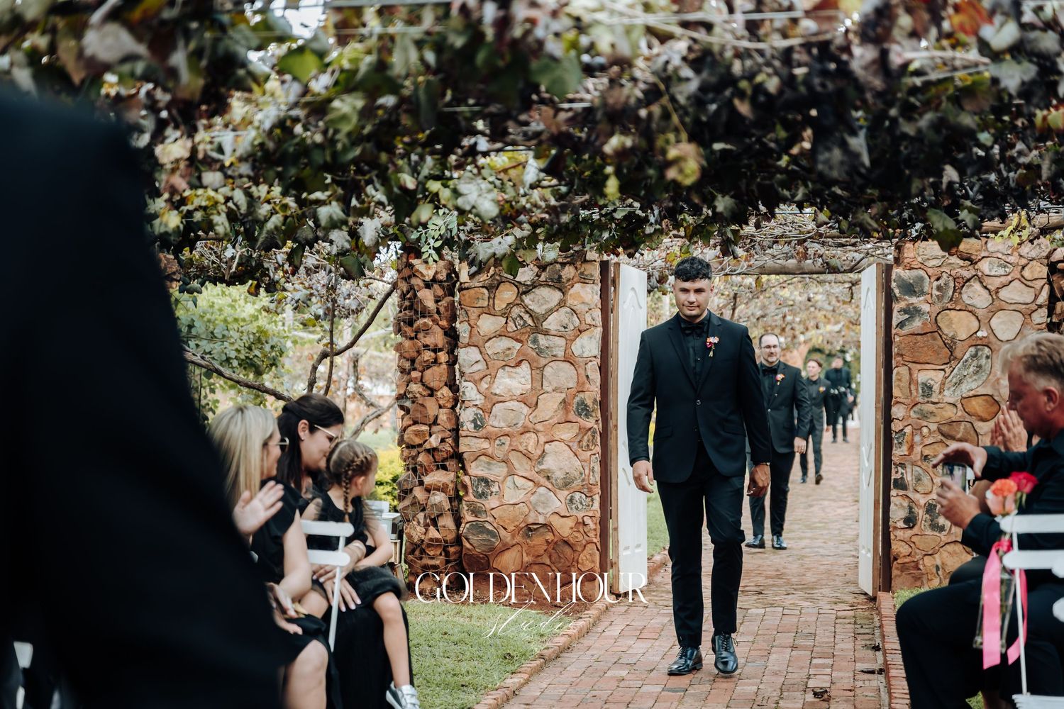 Newlywed couple walks down a brick path surrounded by autumn trees and white fencing.