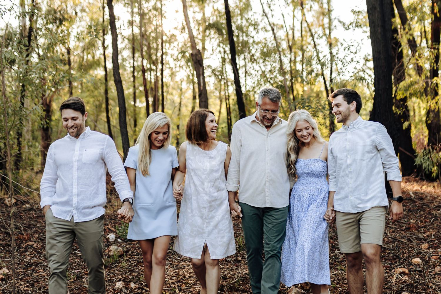 Series of six natural outdoor family portraits in matching white outfits walking through a sunlit forest.
