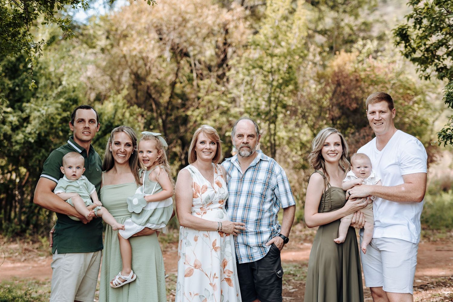 A family photo session outdoors with multiple people wearing coordinated sage green and white outfits.