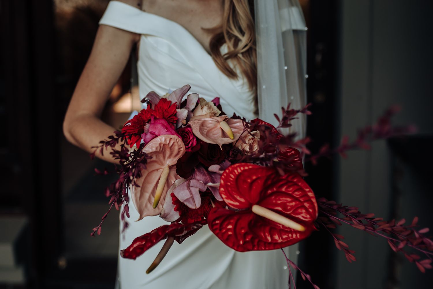 Close-up of dramatic red and pink wedding bouquet against white bridal gown.