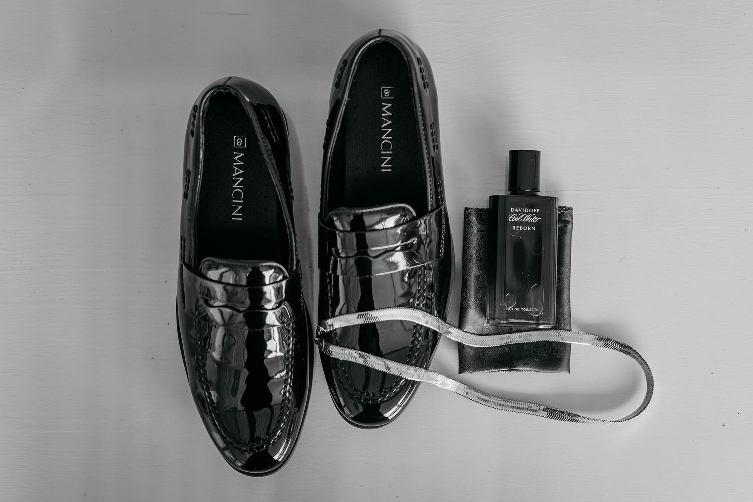 Classic black dress shoes and cologne bottle arranged on light background for formal styling.