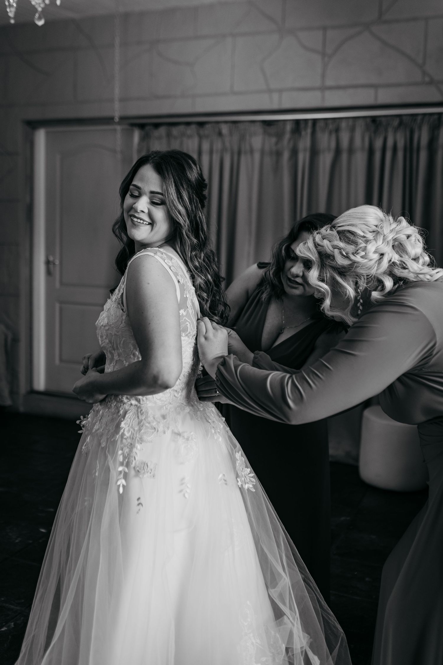 Black and white photo of bride getting her wedding dress adjusted before the ceremony.