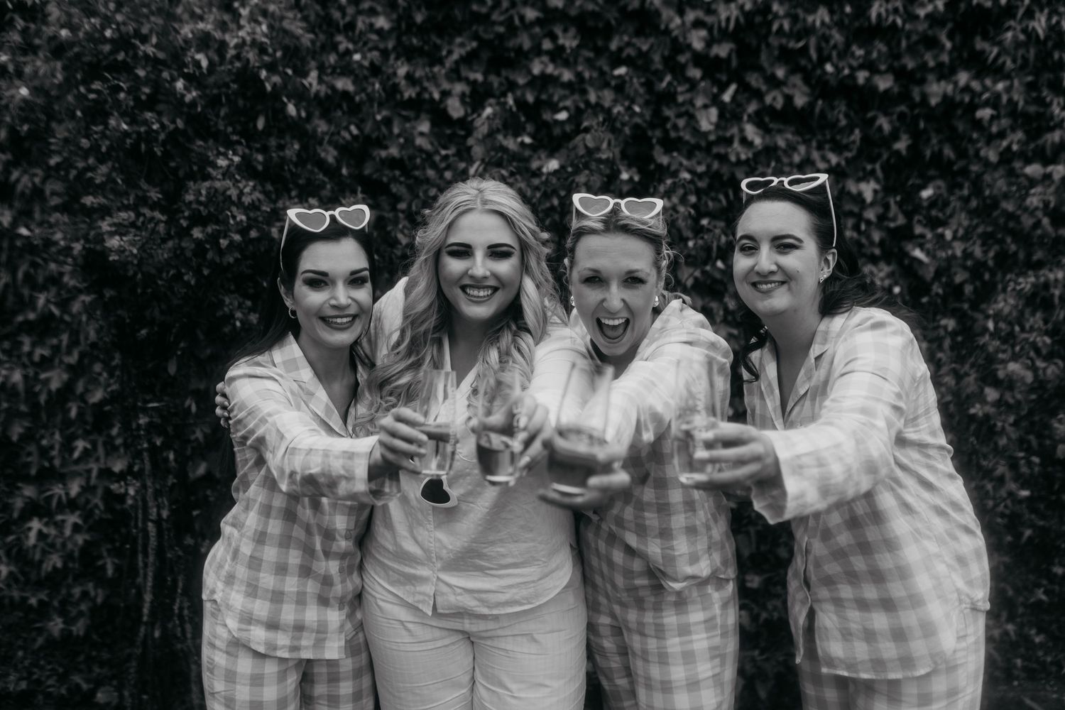 Black and white photo of friends in coordinated outfits toasting with champagne glasses.