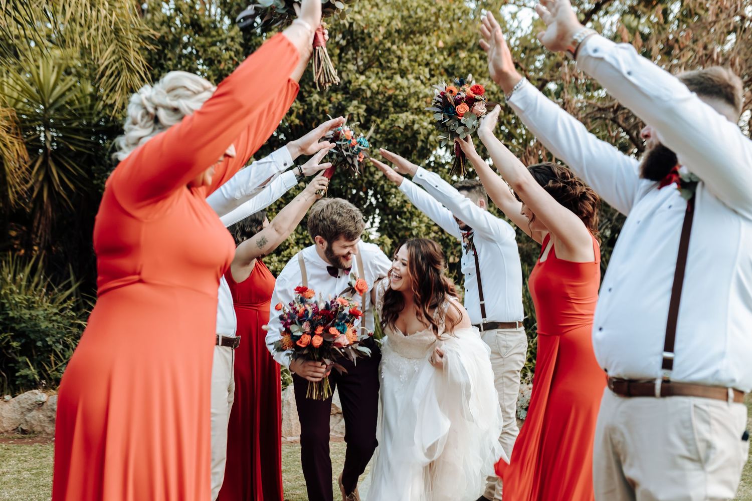 Wedding celebration with bridal party raising arms in celebration under trees.