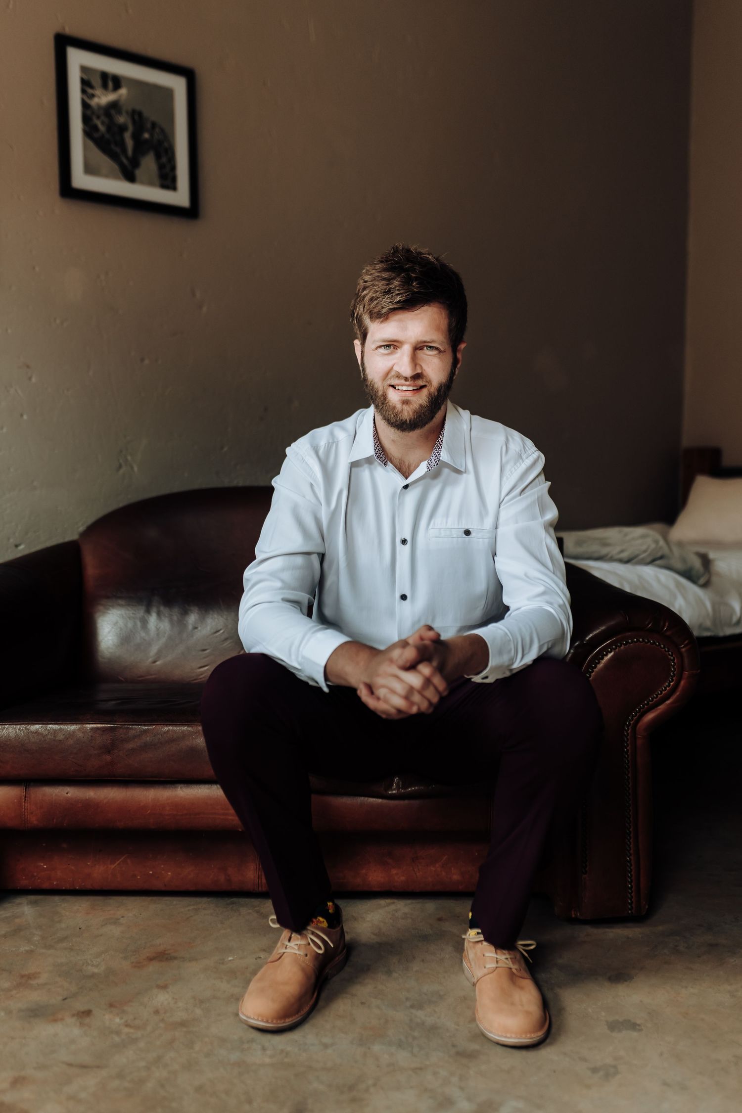 Person in white button-down shirt sitting on brown leather couch in living room.