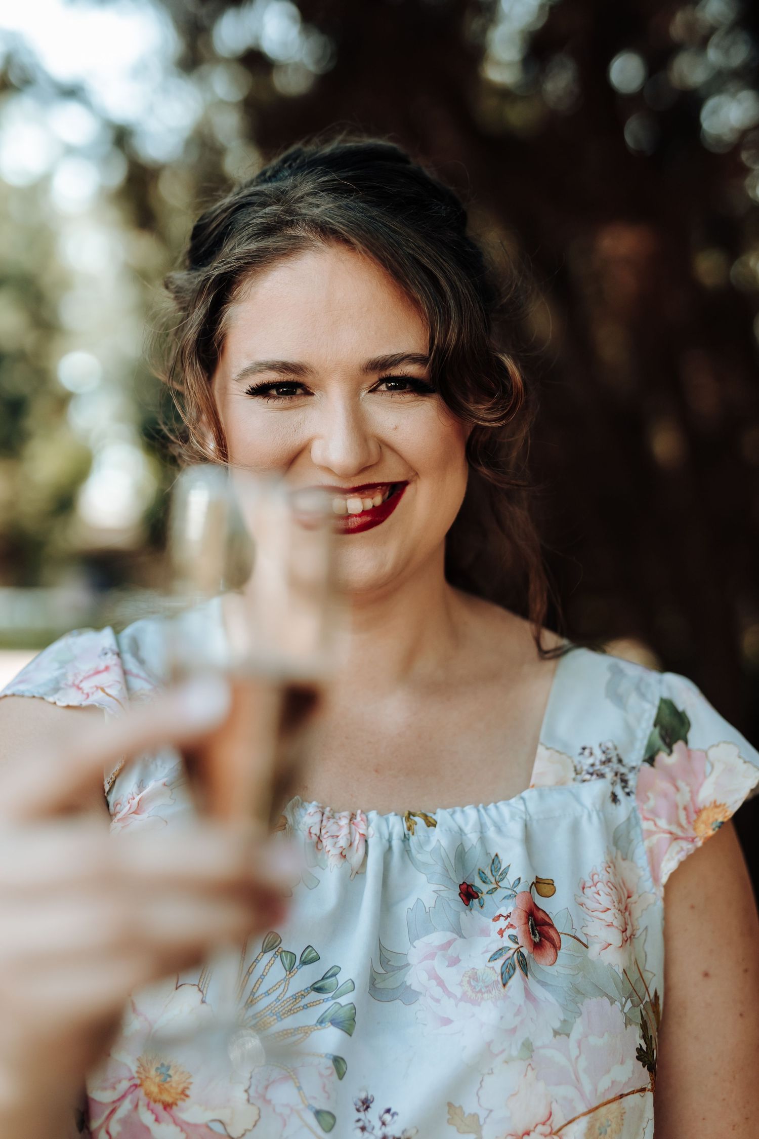 Close-up portrait of someone holding a champagne glass with a blurred natural background.