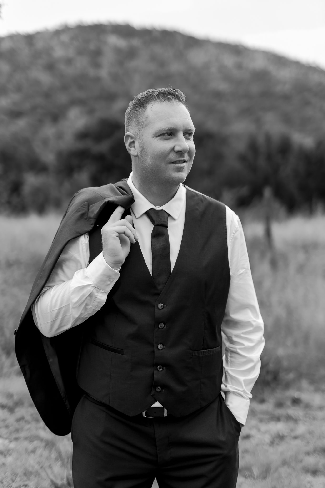 Black and white portrait of groom in vest and tie with casual pose in outdoor setting.