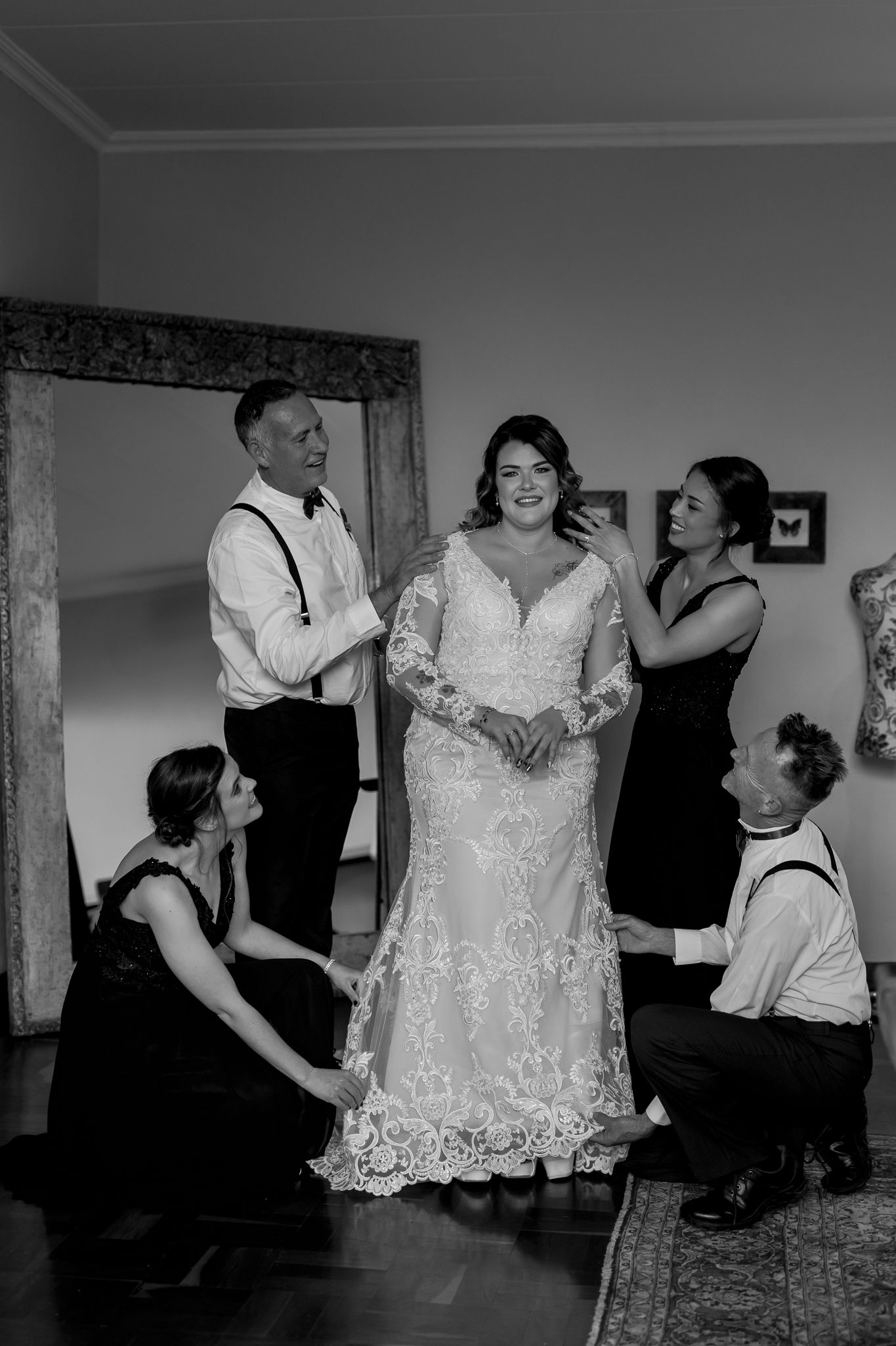Black and white photo shows wedding party helping bride with final dress preparations.