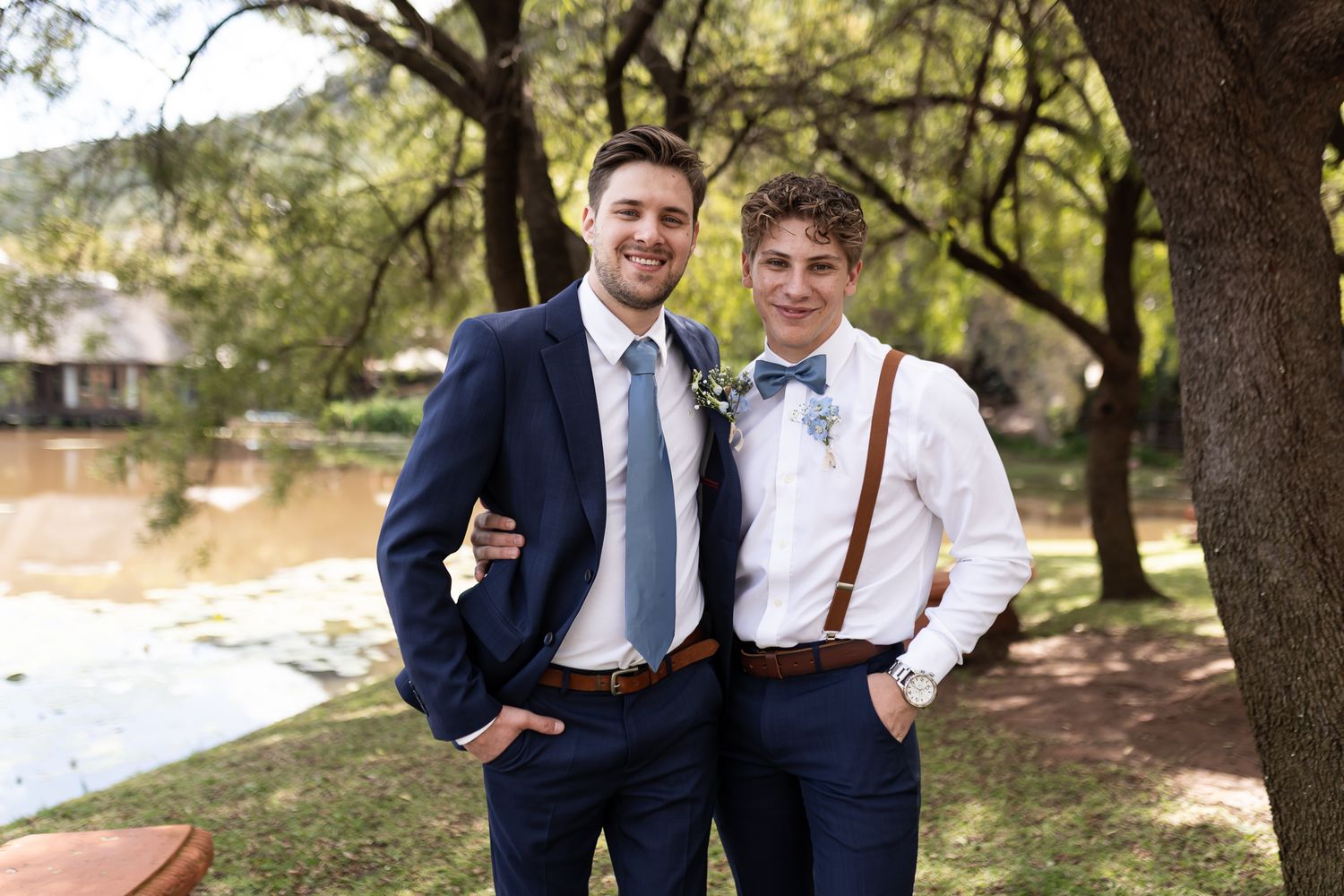 Two groomsmen in complementary formal attire pose together outdoors.