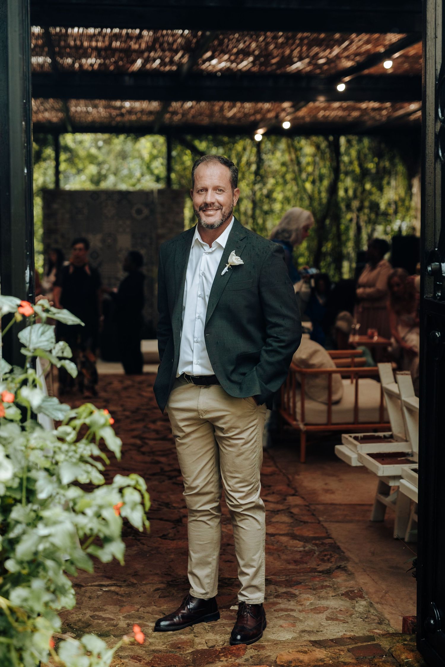 Man in green blazer and khaki pants smiling at an outdoor garden wedding venue.