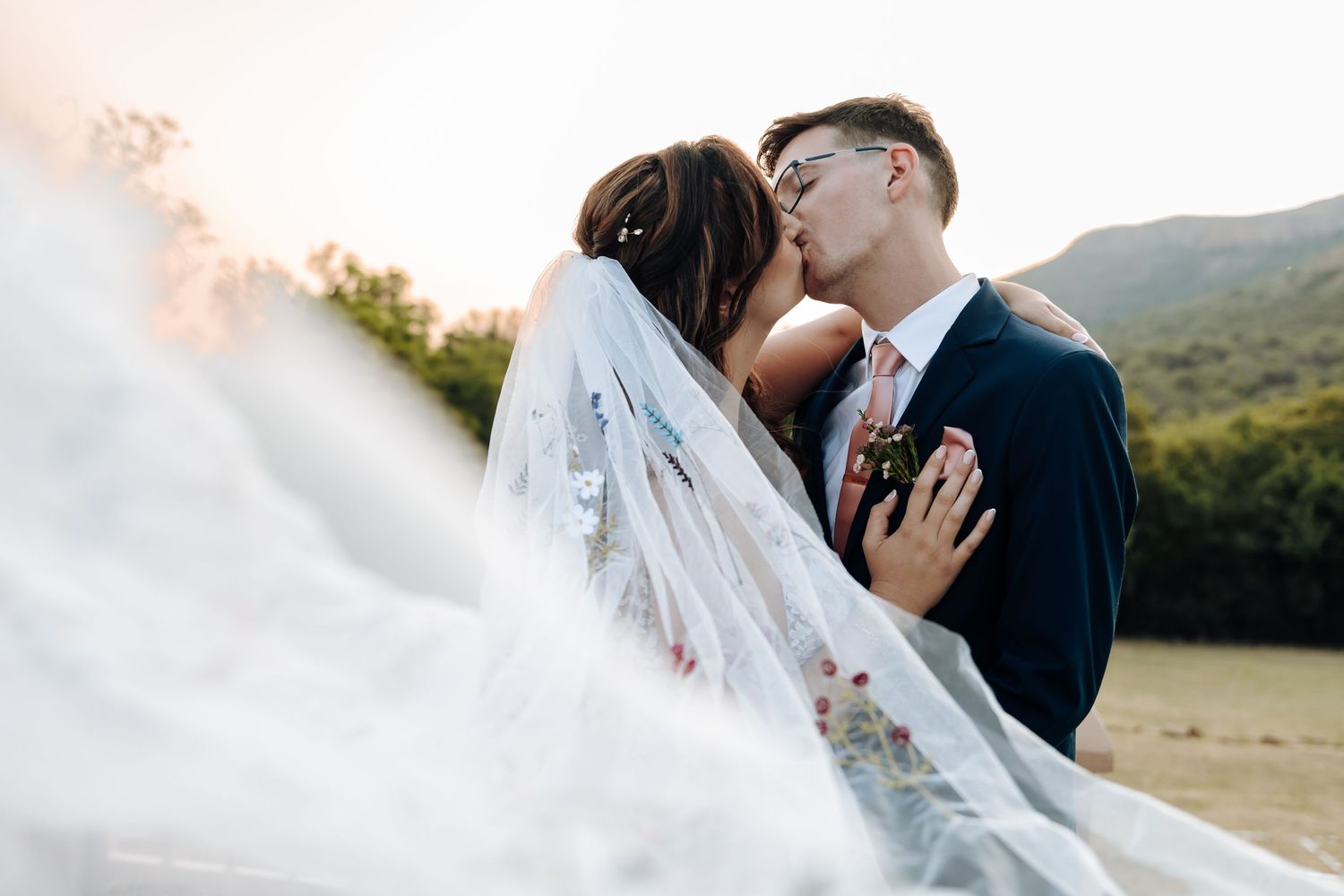 A romantic wedding couple shares an intimate kiss in a scenic mountain setting during golden hour.