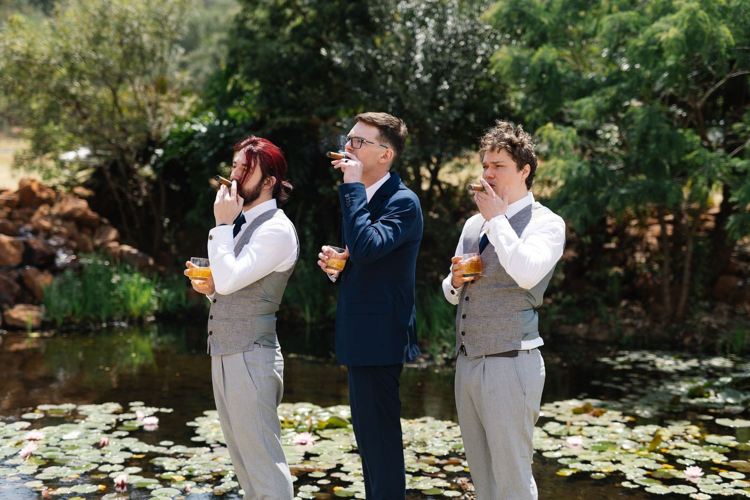Wedding party members in gray and navy attire share first look reactions in an outdoor garden setting.