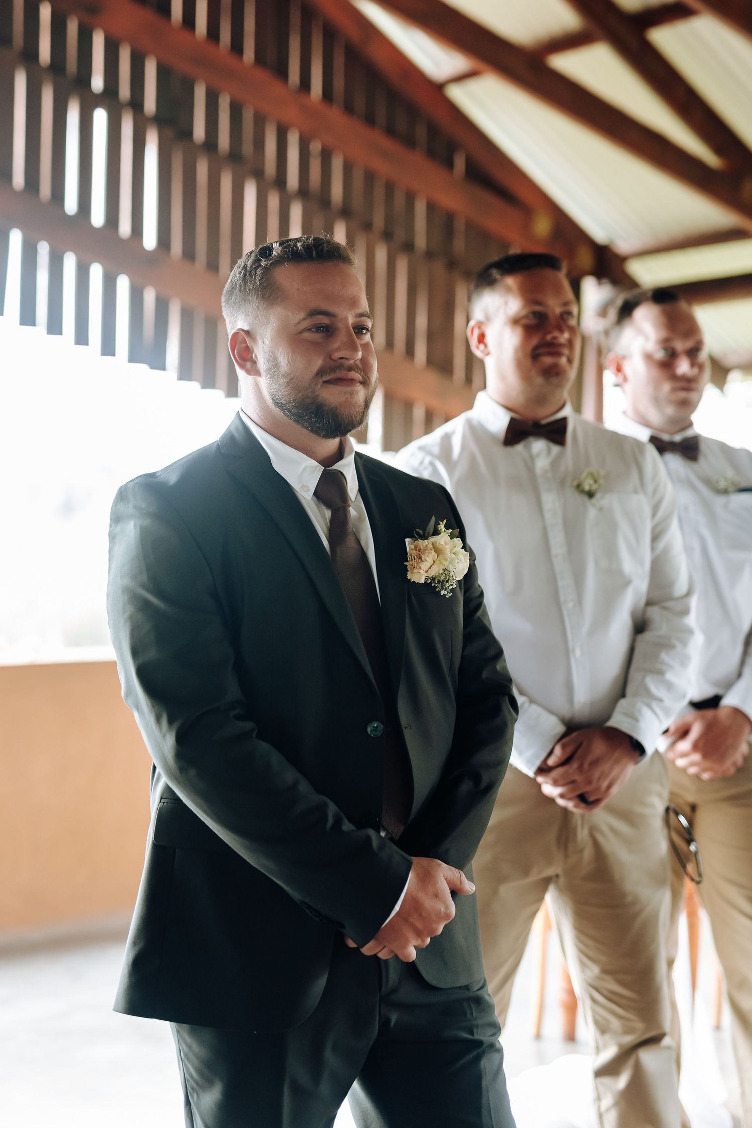 A groom in a black suit stands with groomsmen wearing white shirts and khaki pants at a wedding venue.