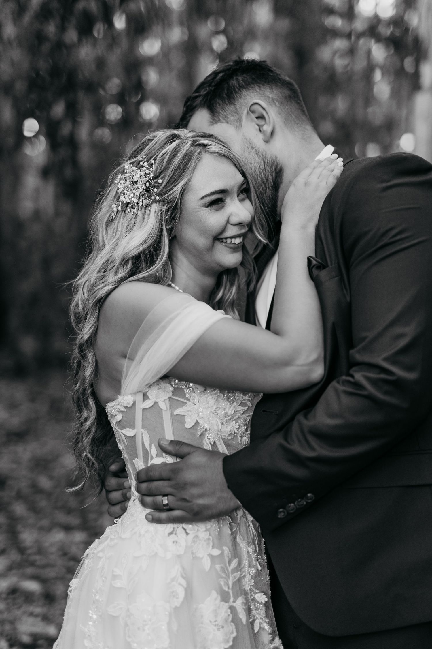 A romantic wedding couple embraces in a moody forest setting with beautiful black and white photography.