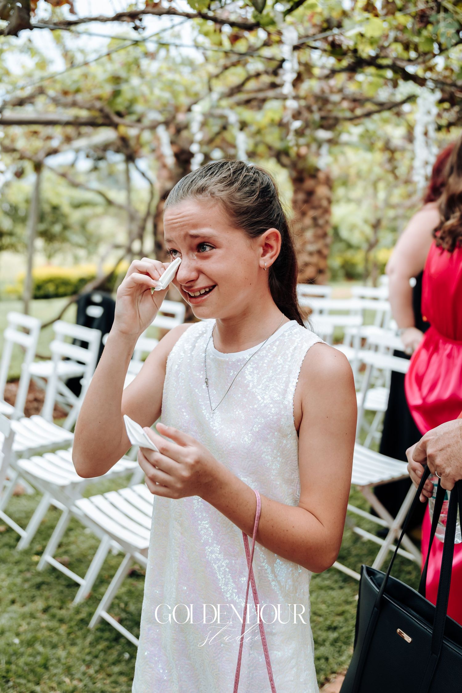 Young attendant in white dress wipes tears during emotional wedding ceremony.