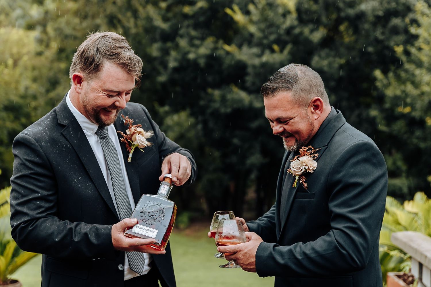 A sequence of photos showing two people in dark suits exchanging gifts and laughing together outdoors.