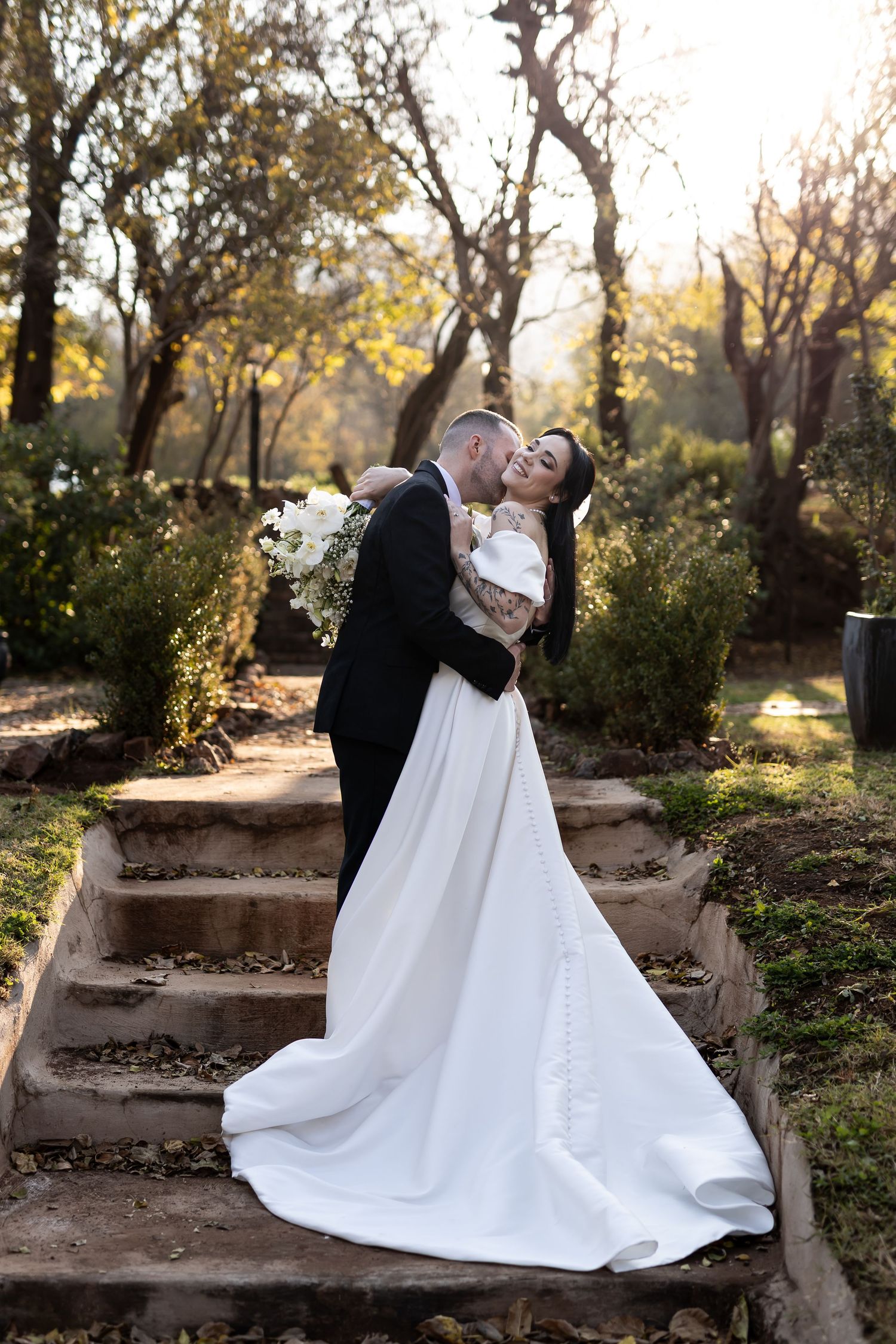 Newlyweds sharing a romantic moment on rustic stone steps surrounded by autumn trees at sunset.