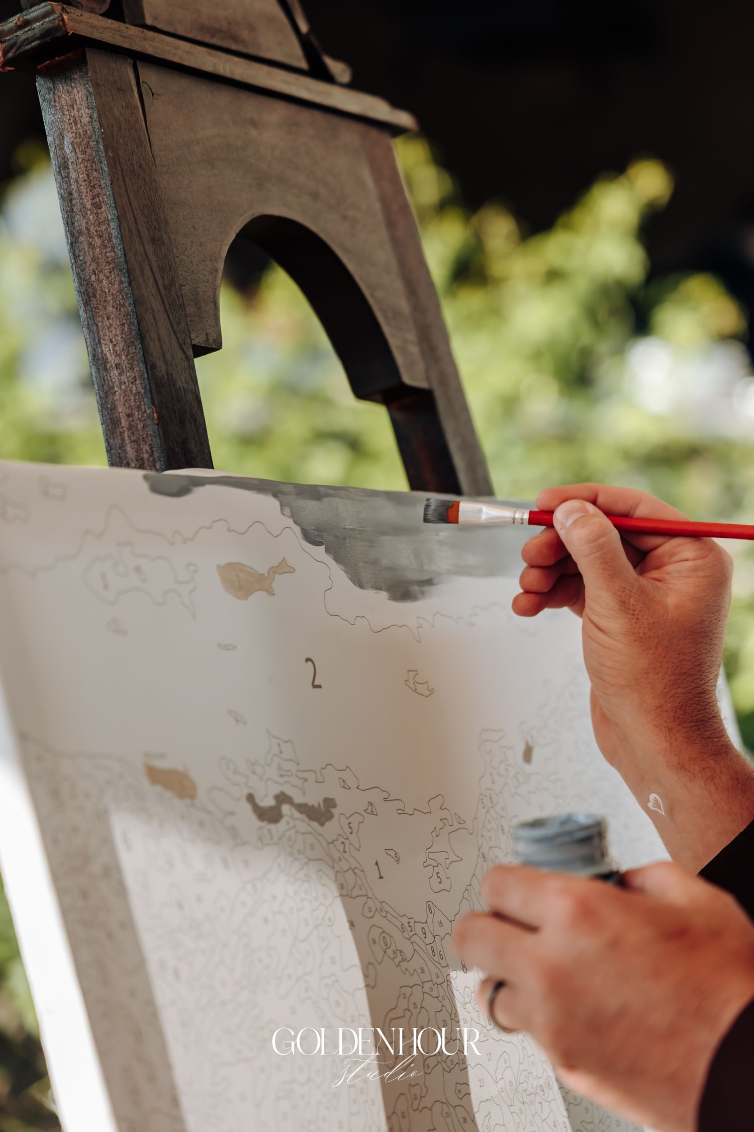 Artist painting on canvas at an outdoor easel during a wedding reception activity.