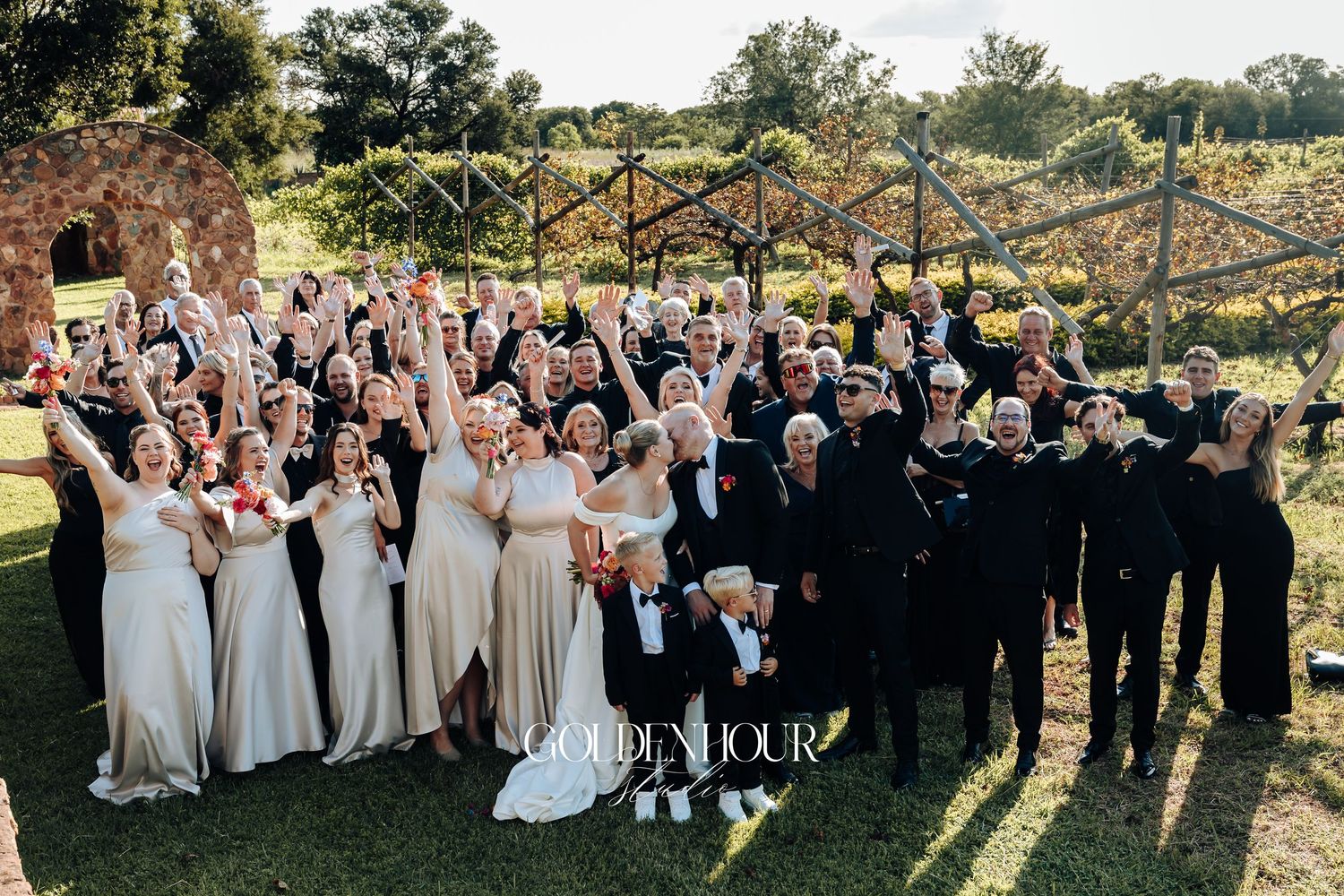 Wedding party poses together outdoors during golden hour sunset for group photos in coordinated formal attire.