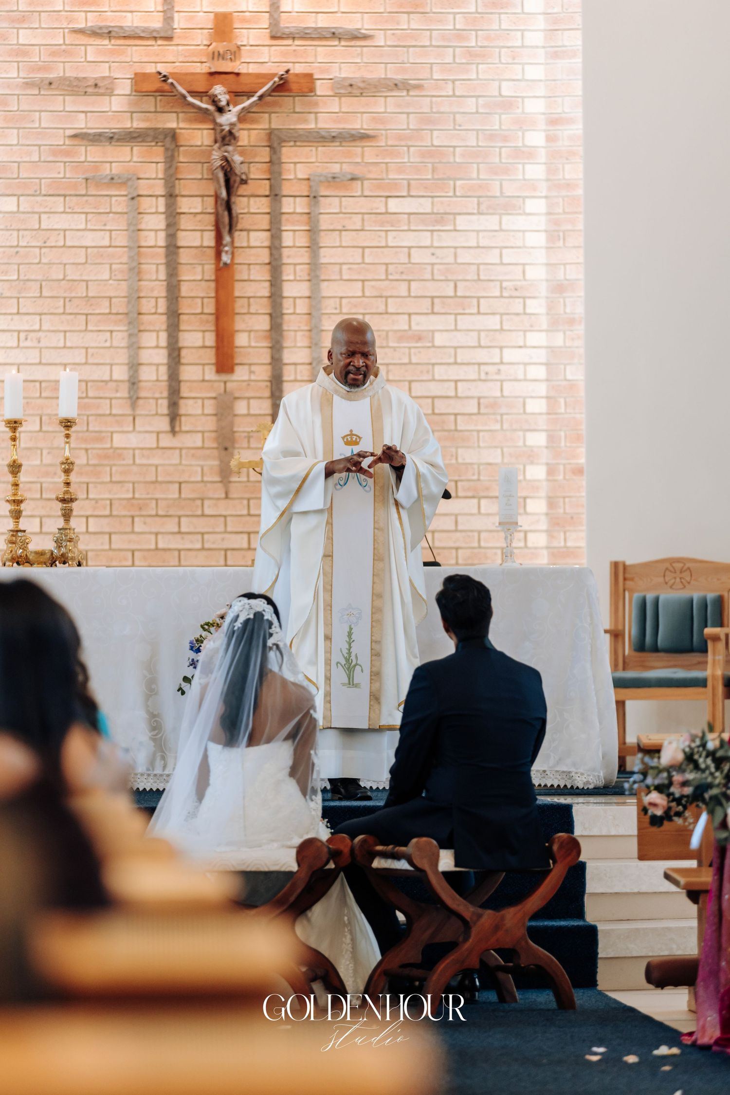Catholic church wedding ceremony with brick walls and crucifix in the background.