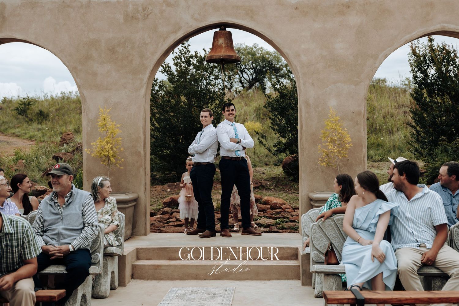 Wedding ceremony guests seated under stone archways at an outdoor venue.
