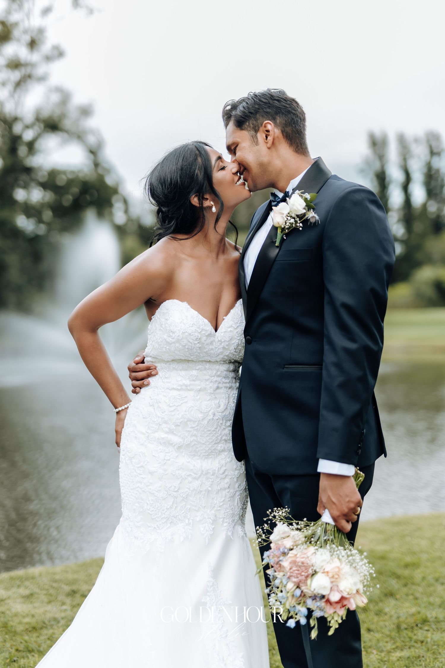 Romantic wedding couple shares intimate moment by lakeside with soft natural lighting.