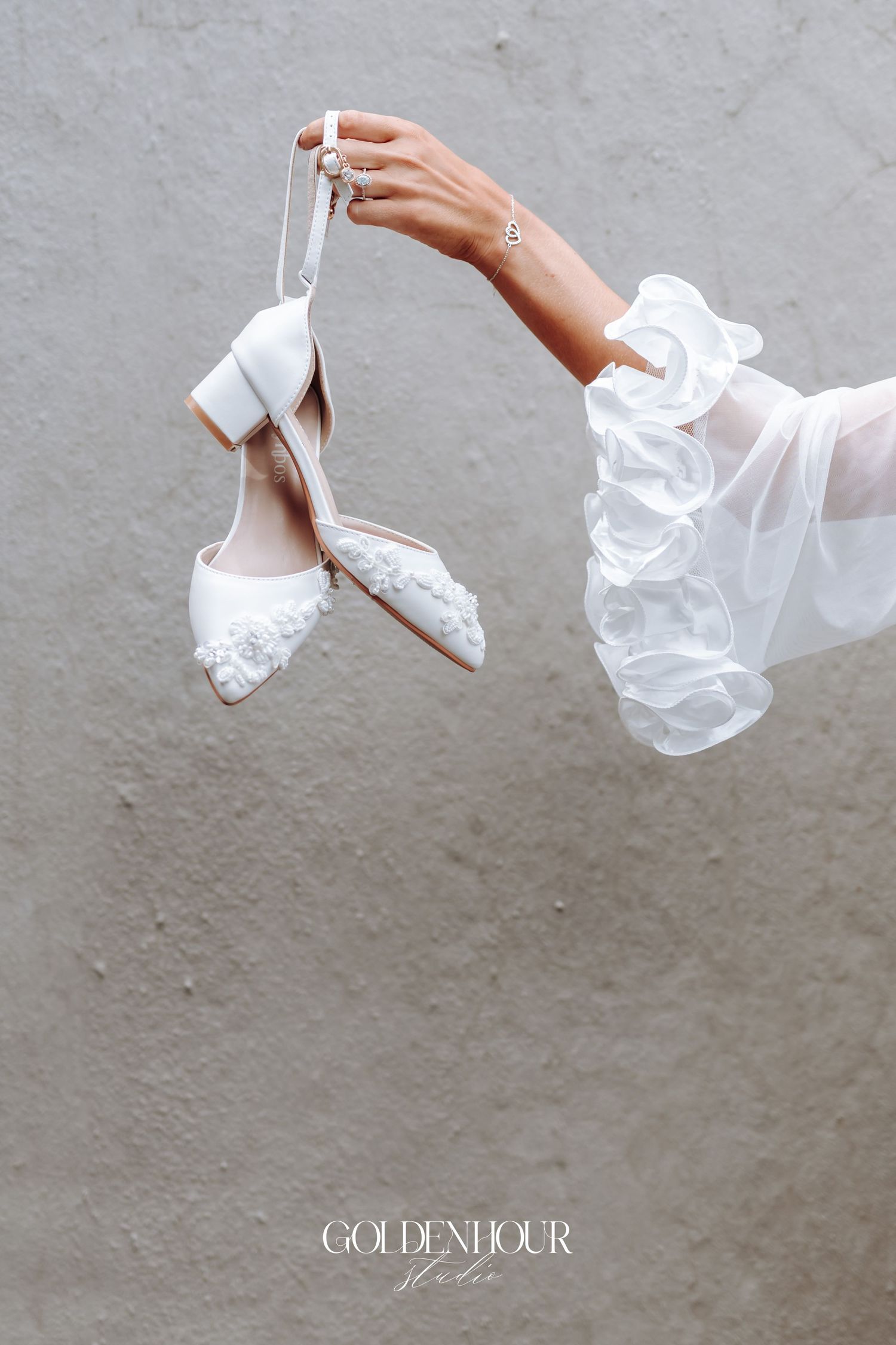 Delicate white bridal shoes and veil being held against a neutral background.