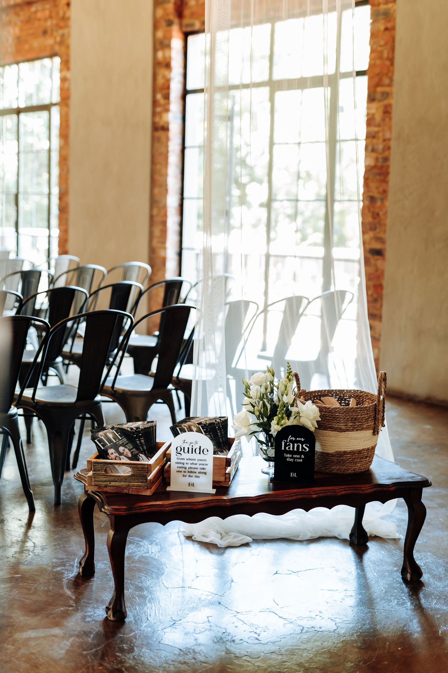 Empty chairs arranged in rows inside a rustic brick-walled venue with natural lighting streaming through windows.