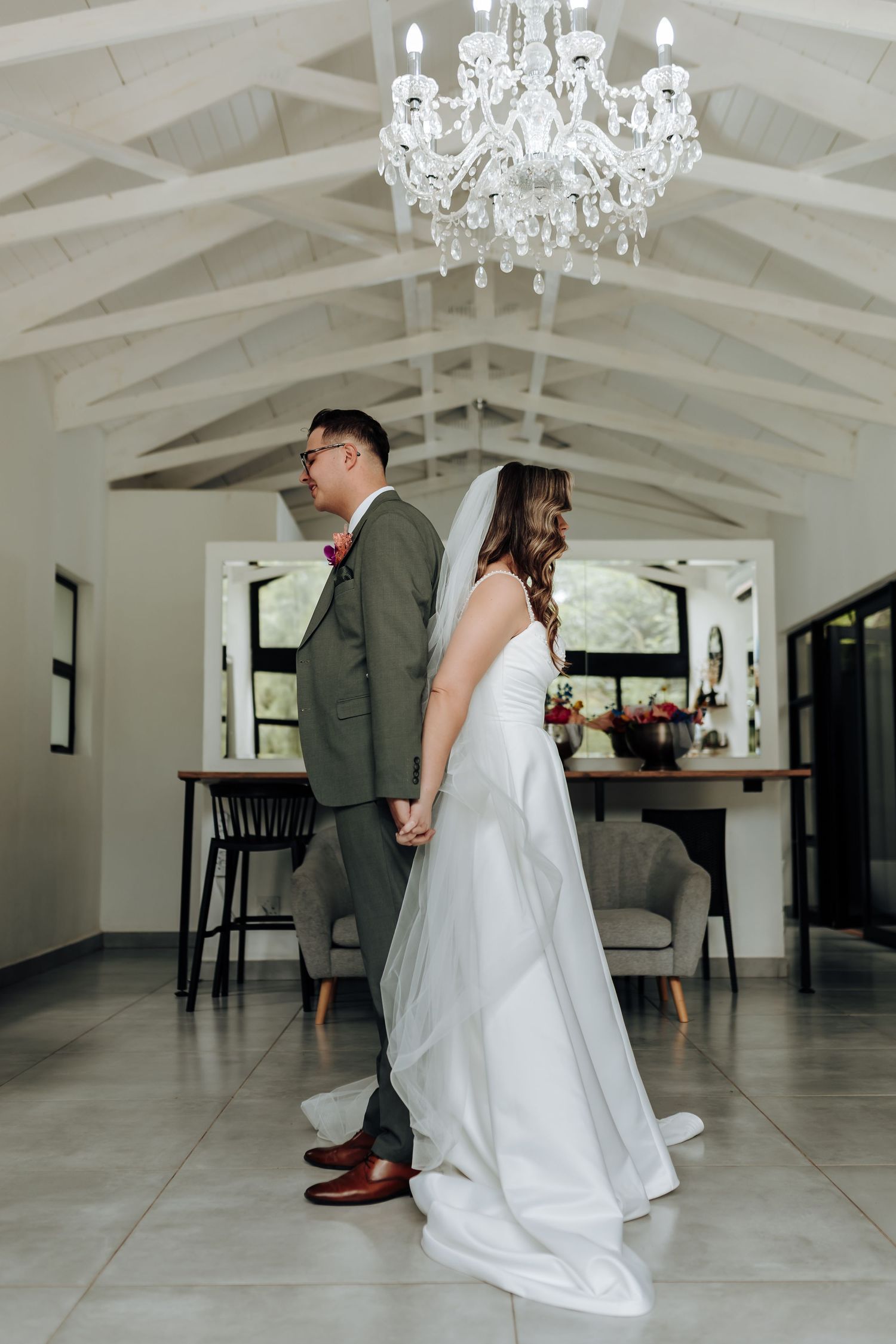 First look wedding moment captured under crystal chandeliers in modern white space.