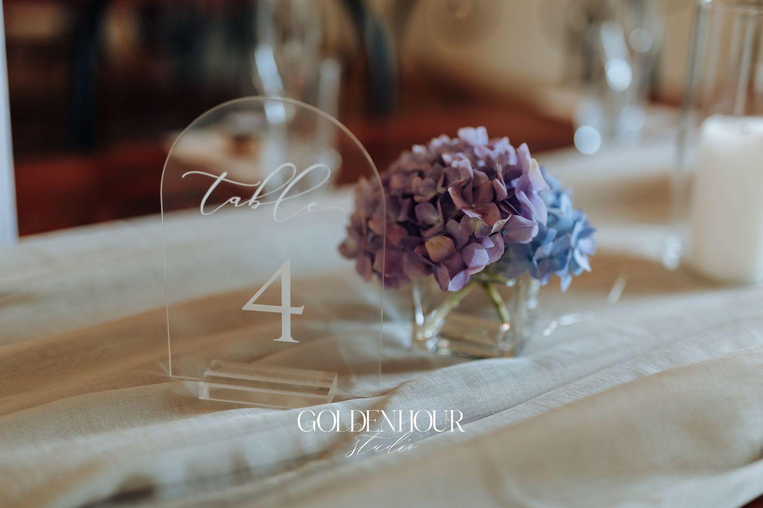 Elegant table settings with purple floral centerpieces and white linens in a wedding reception venue.
