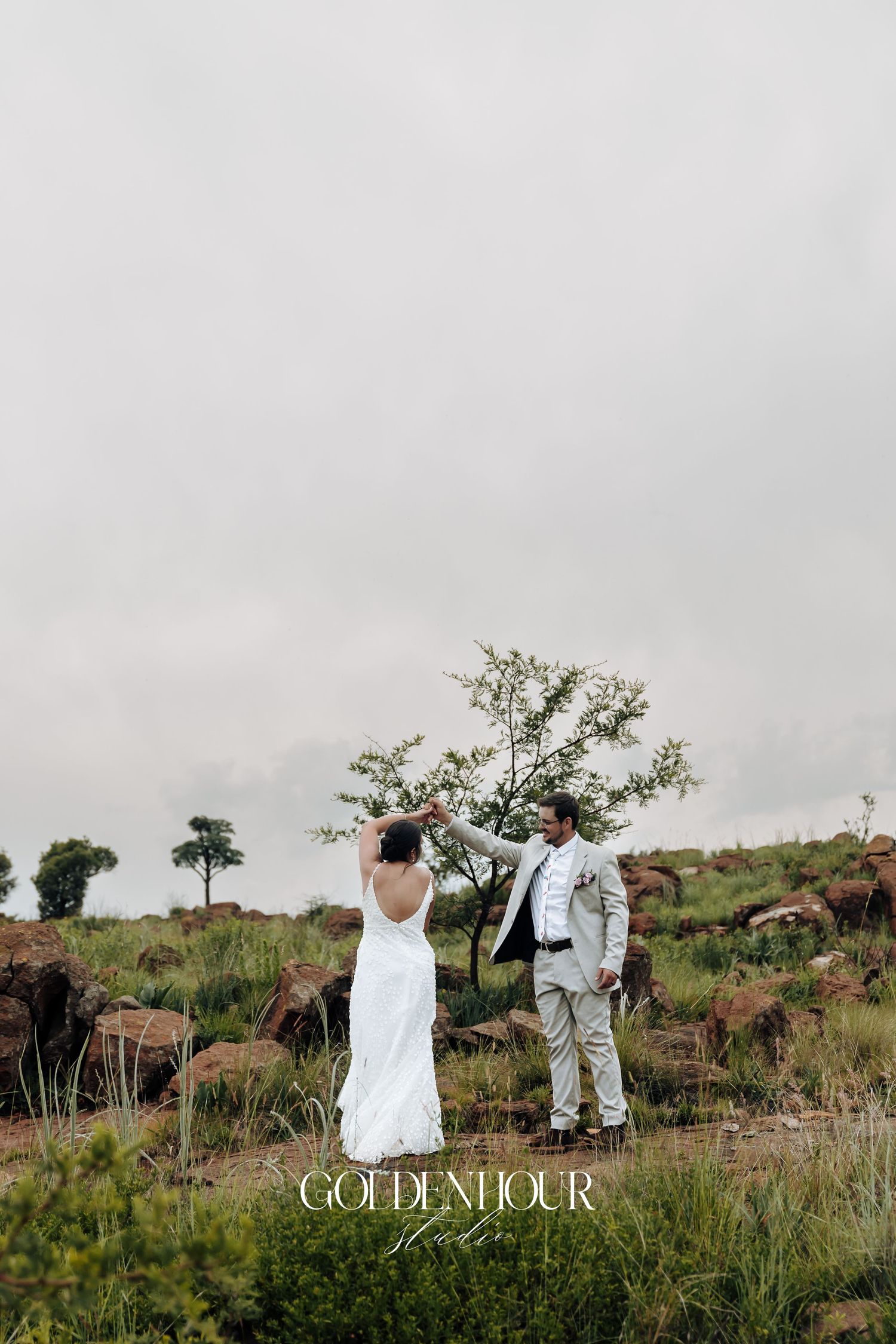 Couple stands together on hilltop against cloudy sky in wedding attire.