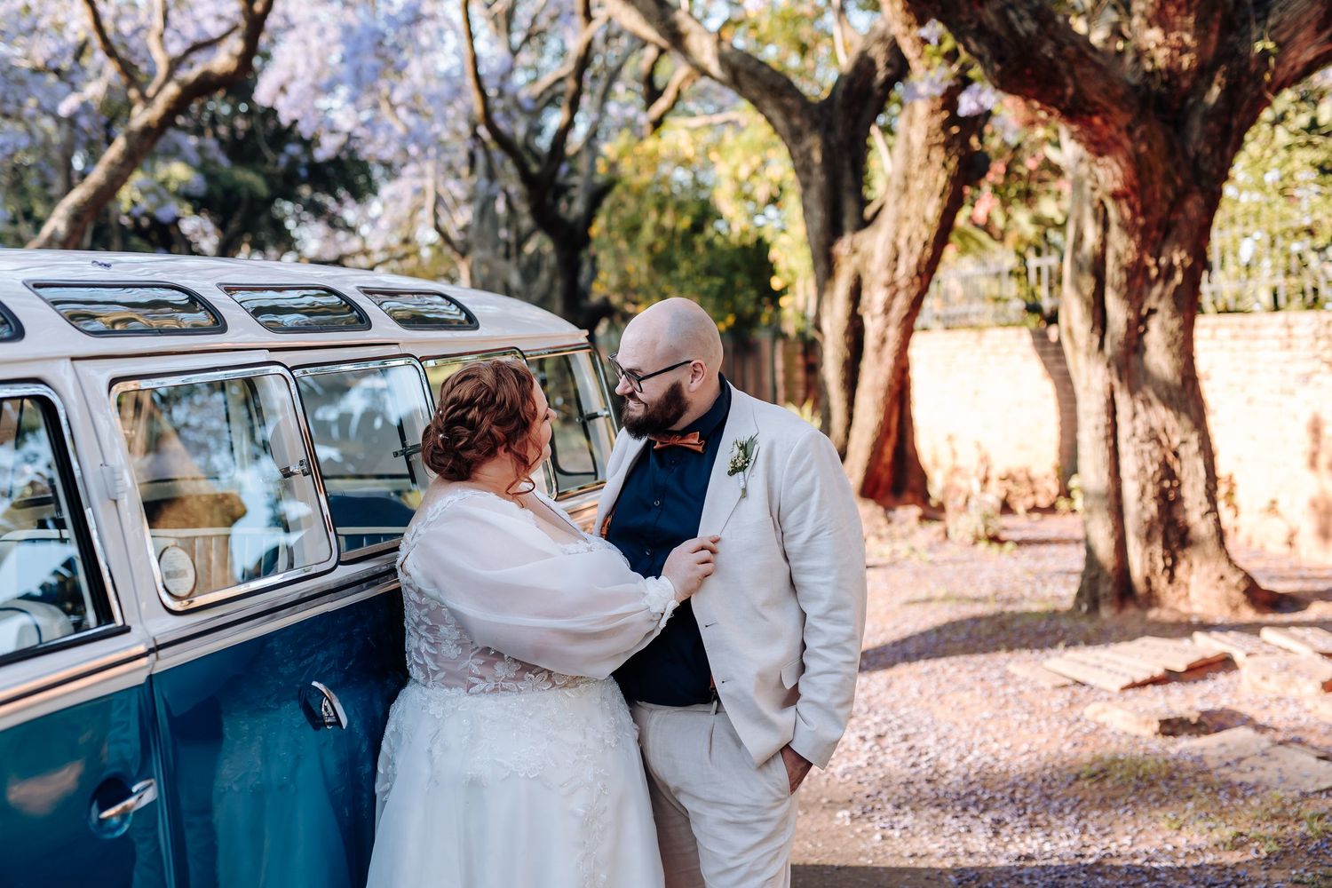 A vintage classic car parked under trees creates a romantic backdrop for a wedding photo session.