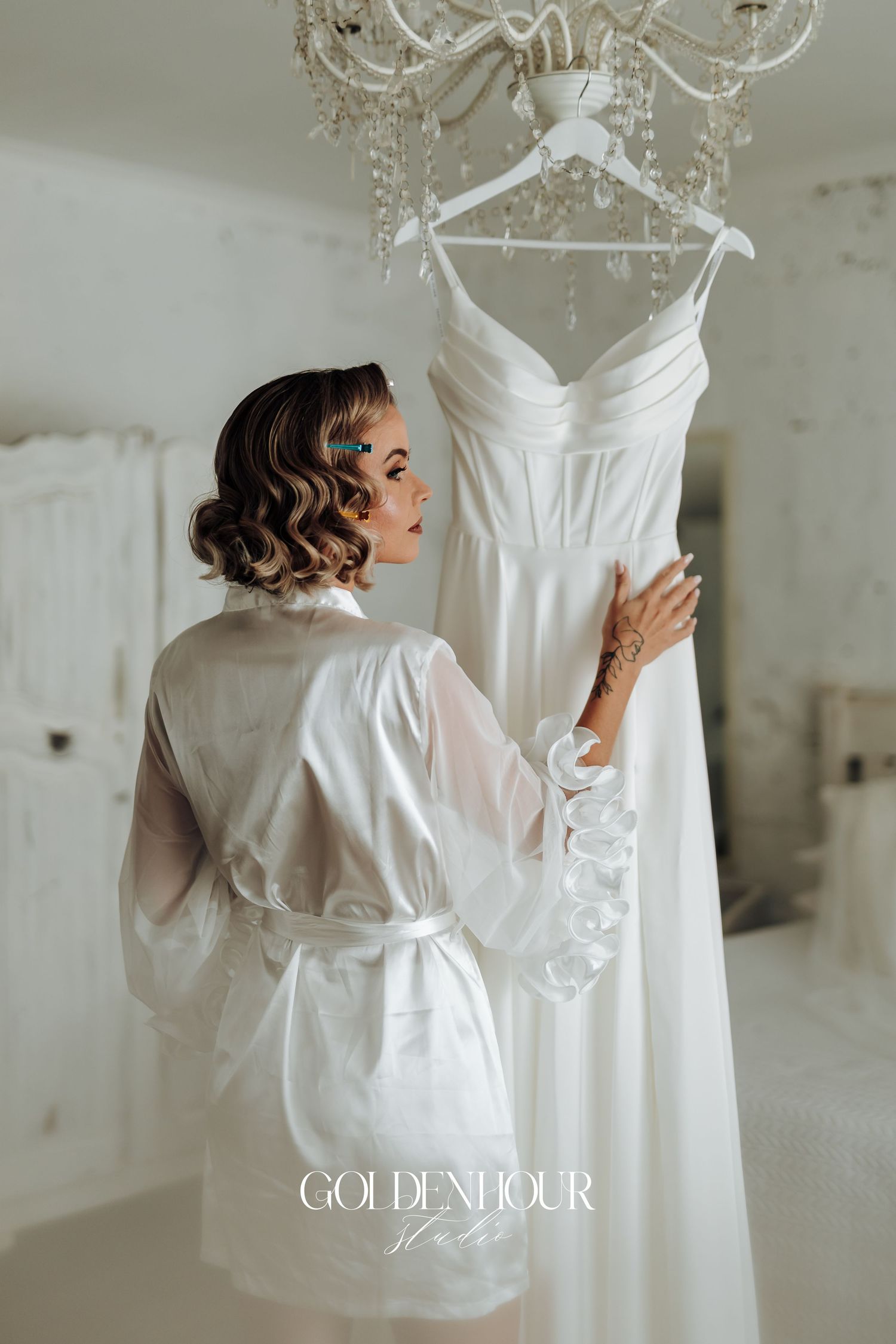 A bride in a white robe admires her wedding dress hanging on display before the ceremony.