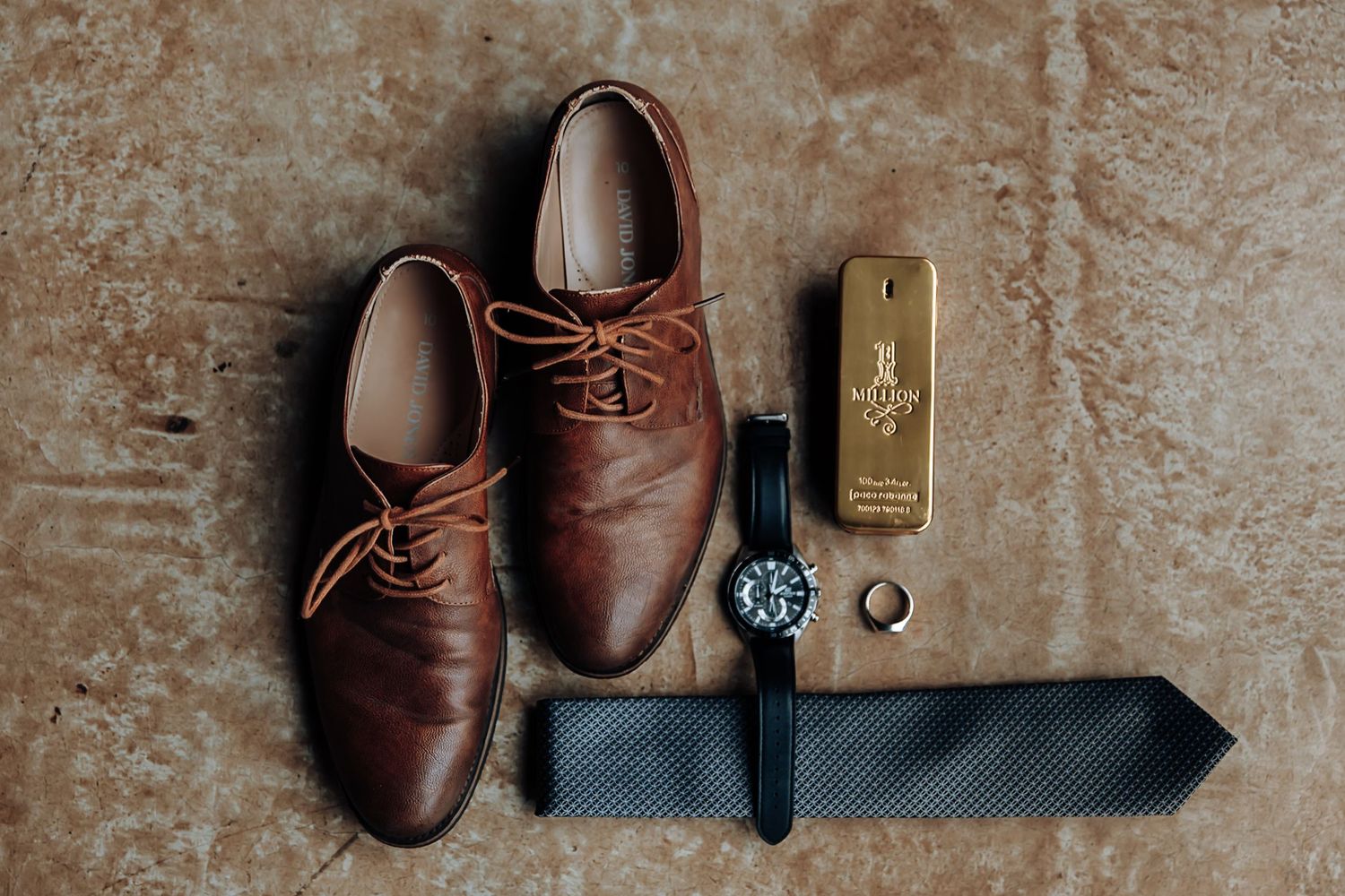 A collection of vintage brown leather shoes and accessories arranged artistically on a textured beige background.