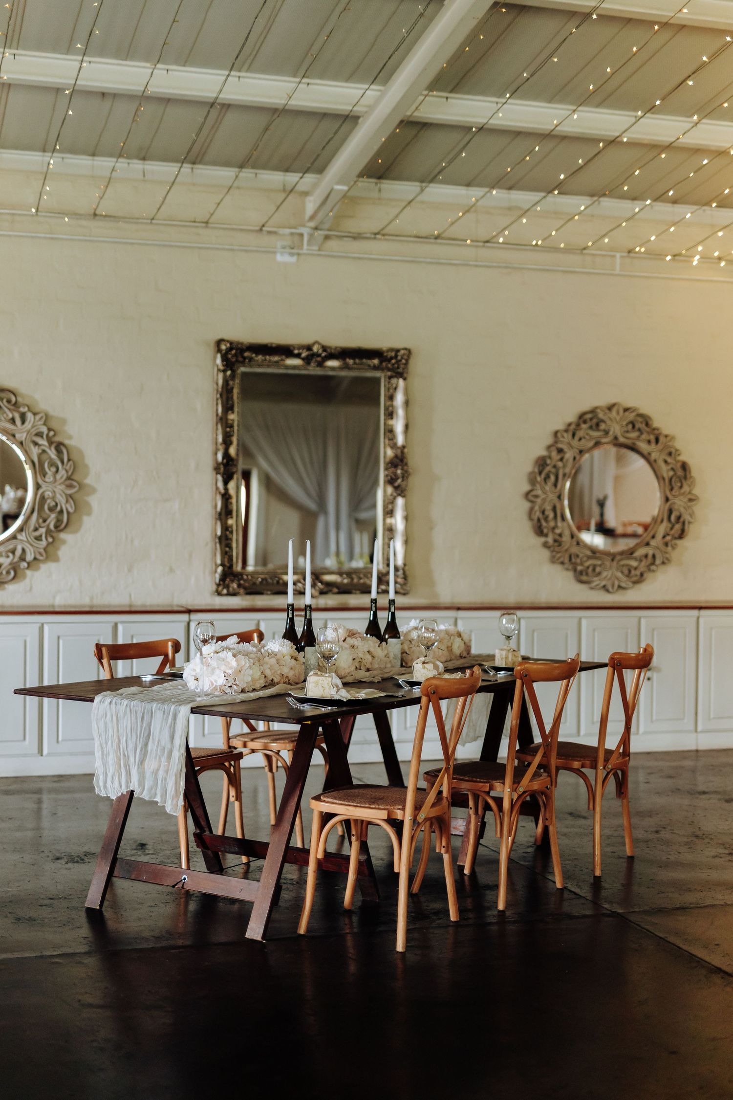 Elegant dining room setup with wooden tables and ornate wall mirrors in a rustic-modern event space.