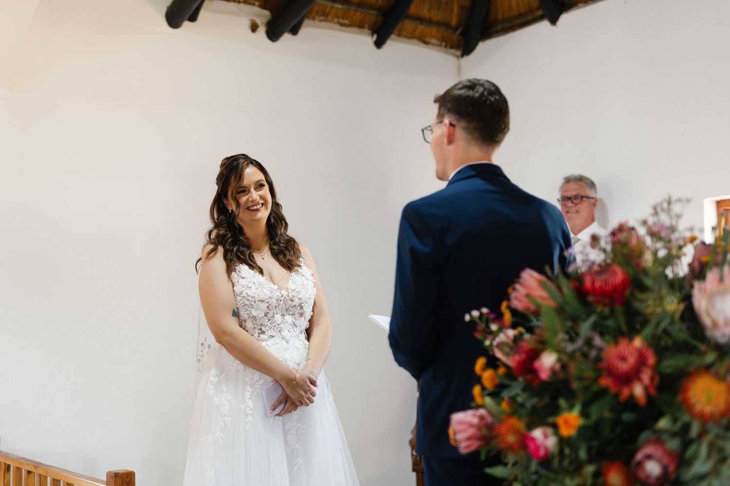 A wedding ceremony takes place in a rustic venue with exposed wooden beams and colorful floral arrangements.