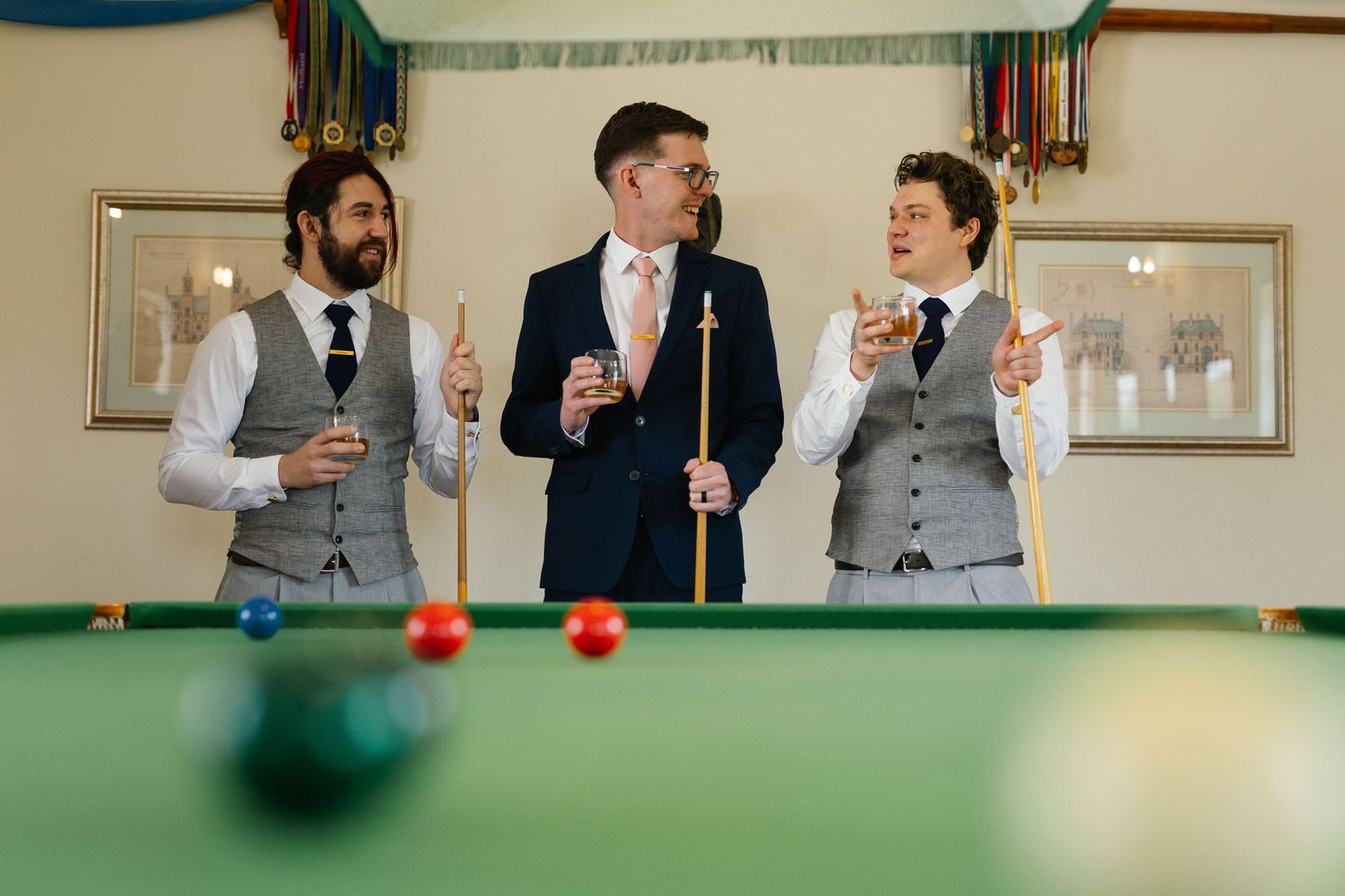 A group of people in formal attire gather around a pool table during what appears to be a wedding celebration.