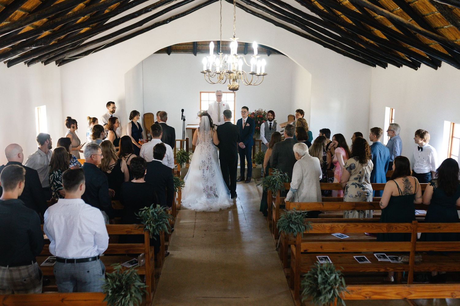 Military service members attend a wedding ceremony in a modern chapel with dramatic angled wooden beams overhead.